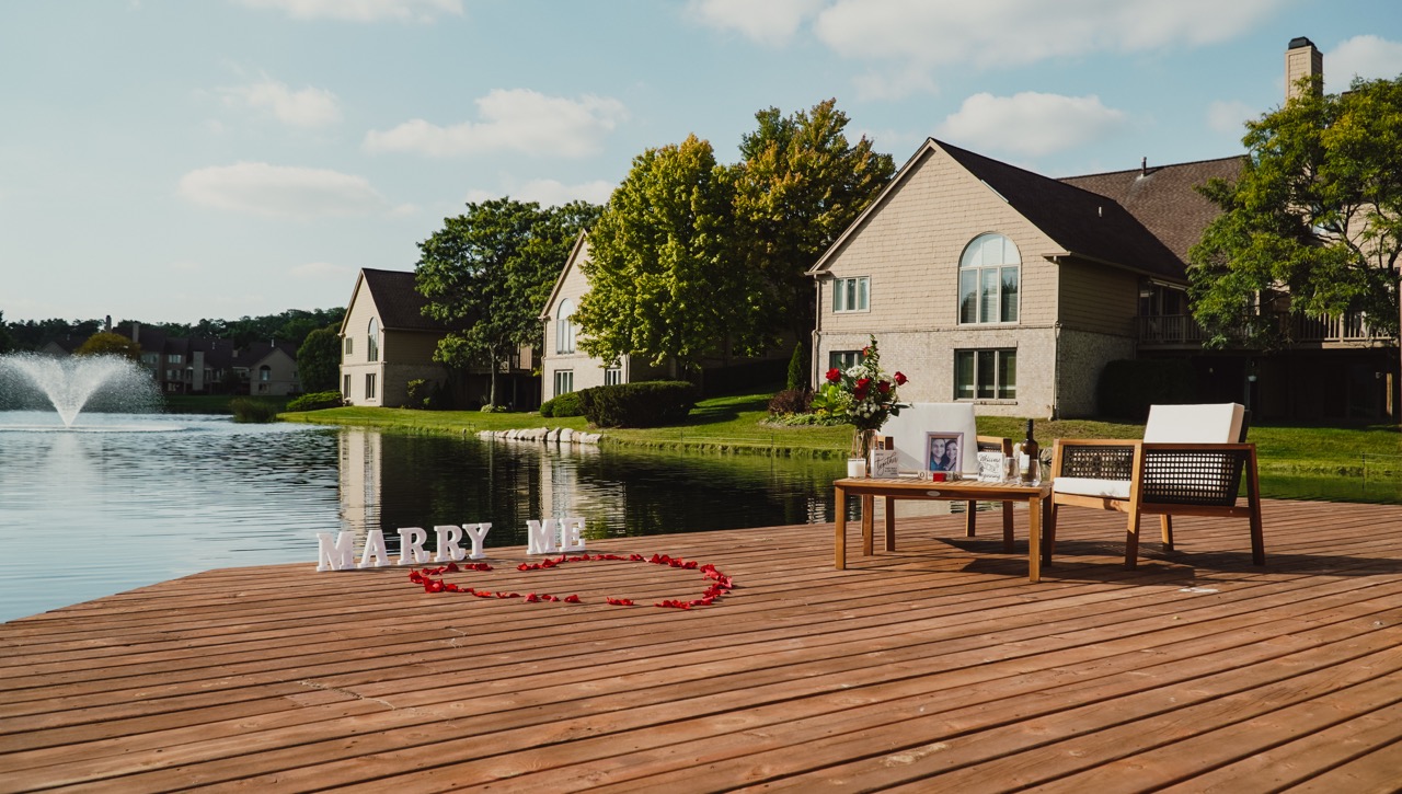A lakeside proposal setting with flowers and Marry Me letters